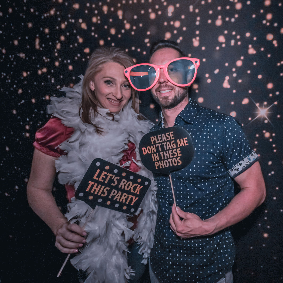 Couple posing with props in front of a sparkle backdrop